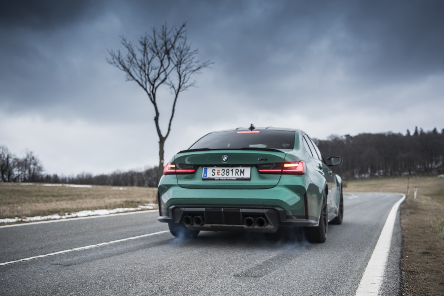 Ein grüner BMW M3 lässt auf einer Landstraße die Hinterräder durchdrehen, sodass etwas Qualm sichtbar wird.