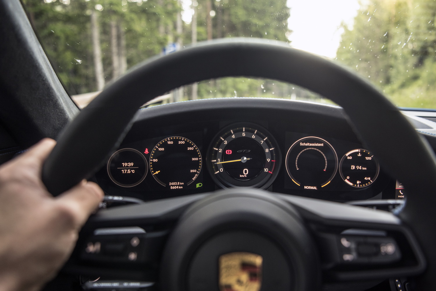 Eine Hand greift auf das Lenkrad des Porsche 911 GT3, hinter dem sich die teildigitalen Armaturen befinden.