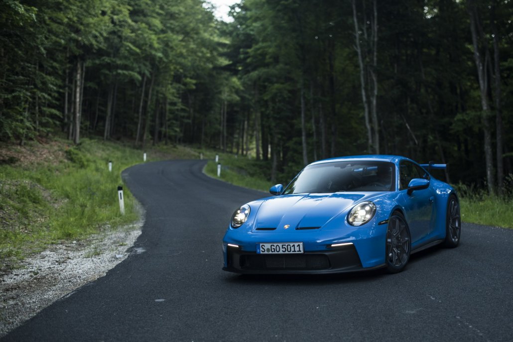 Ein blauer Porsche 911 GT3 steht quer über einer Straße im Wald.