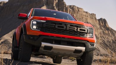Ein orangener Ford Ranger Raptor 2022 steht vor einem felsernen Hügel in der Wüste.