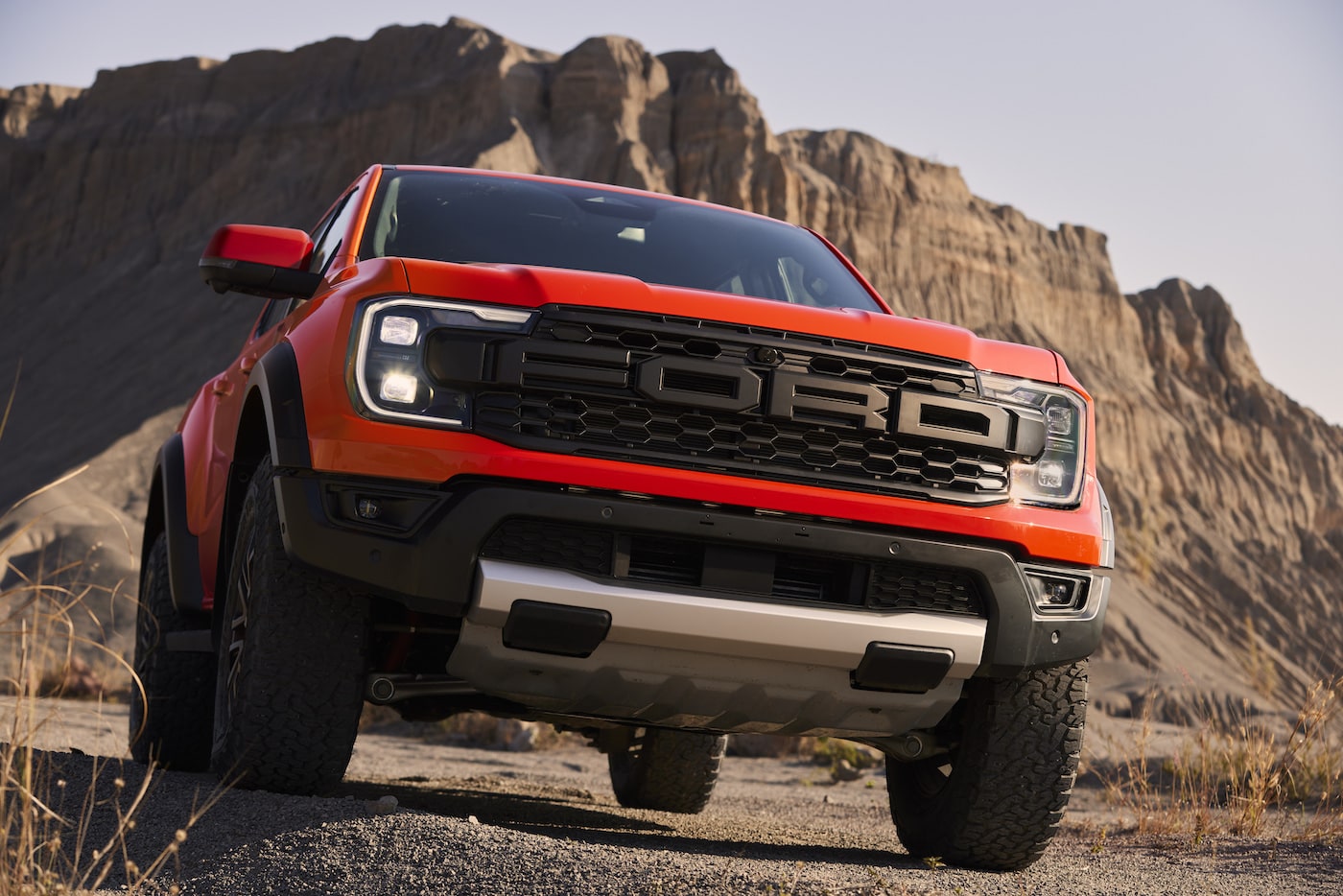 Ein orangener Ford Ranger Raptor 2022 steht vor einem felsernen Hügel in der Wüste.