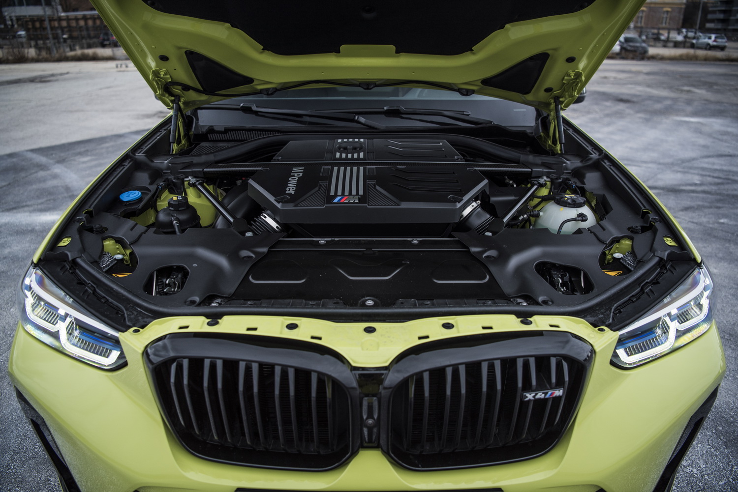 Die Motorhaube eines gelben BMW X4 M ist geöffnet und gibt den Blick frei auf den Reihensechszylinder.