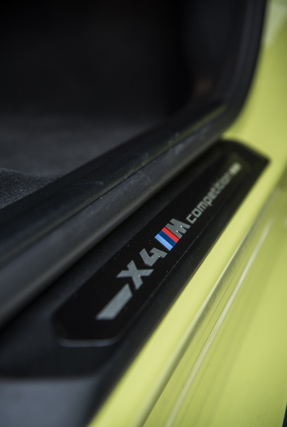 Der Schriftzug X4 M Competition ist auf der Einstiegsleiste eines gelben SUV-Coupés zu sehen.