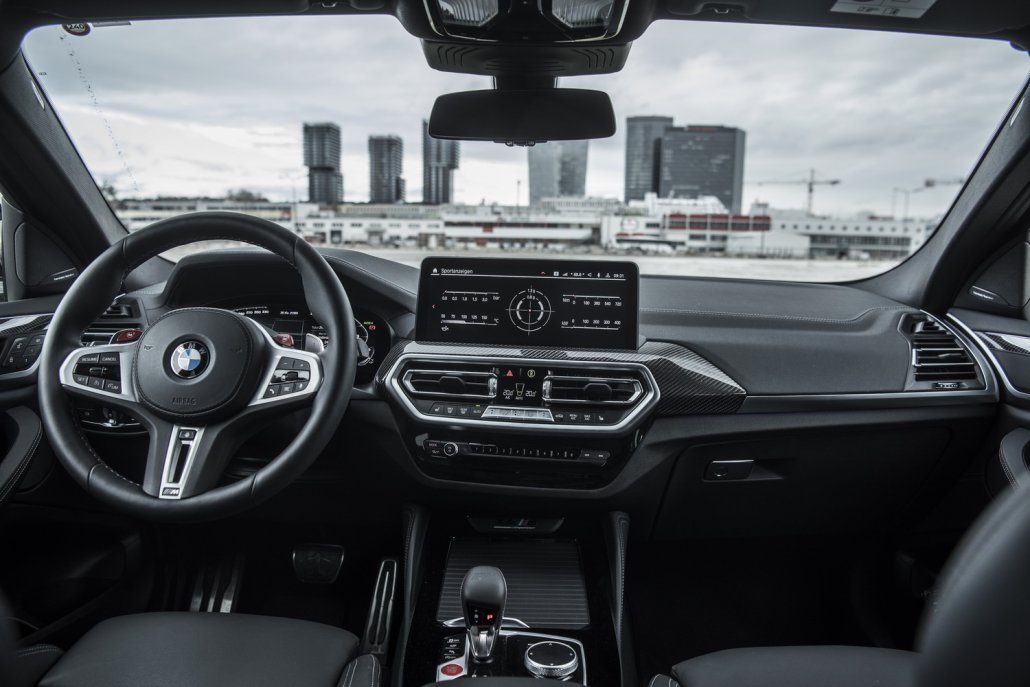 Das Cockpit eines gelben BMW X4 M Competition mit schwarzem Leder, Carbon-Applikationen und zwei Displays..