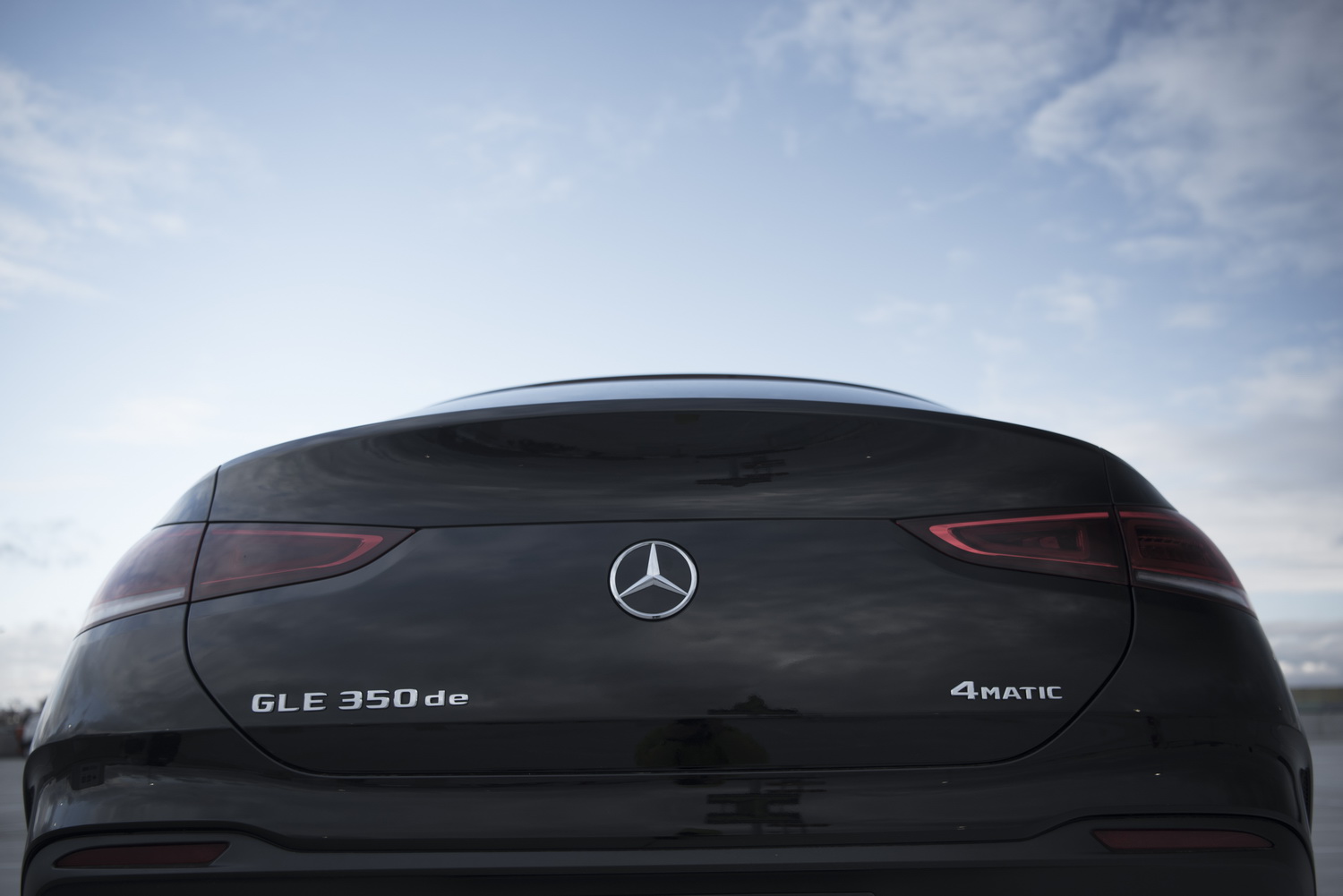 Silberne Schriftzüge und das Markenlogo am Heck des schwarzen Mercedes GLE 350 de, der auf einem Parkdeck unter blauem Himmel steht.