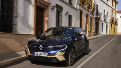 Ein dunkelblauer Renault E-Tech Electric fährt auf einer Straße in der Stadt mit Häusern im Hintergrund.