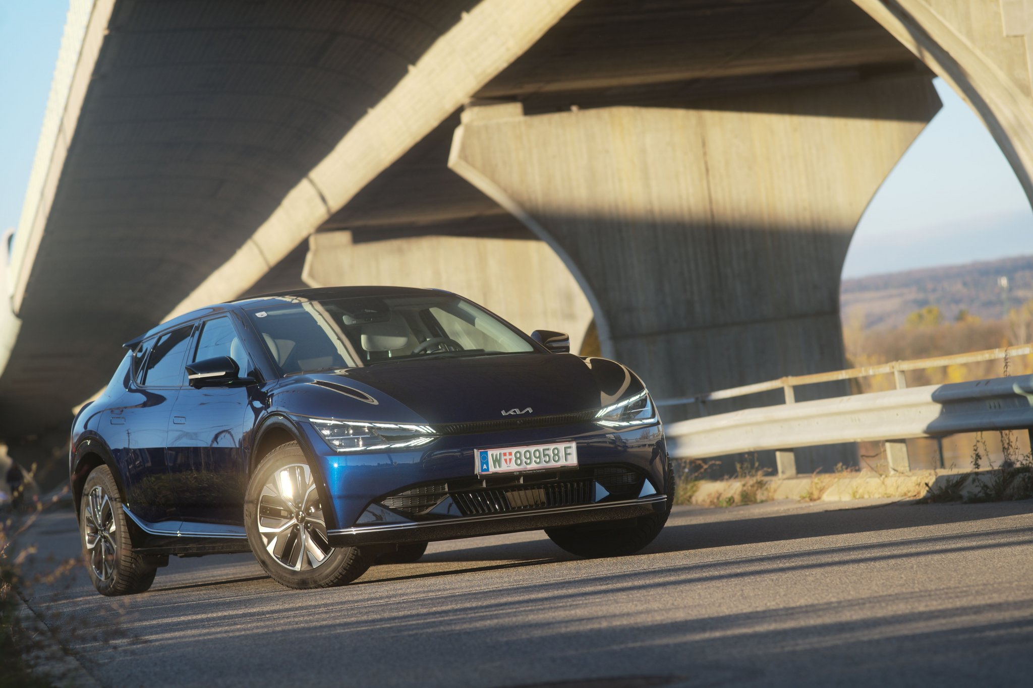 Ein blauer Kia EV6, das Car of the Year 2022, steht auf einer Straße unter einer großen Brücke an einem sonnigen Tag.