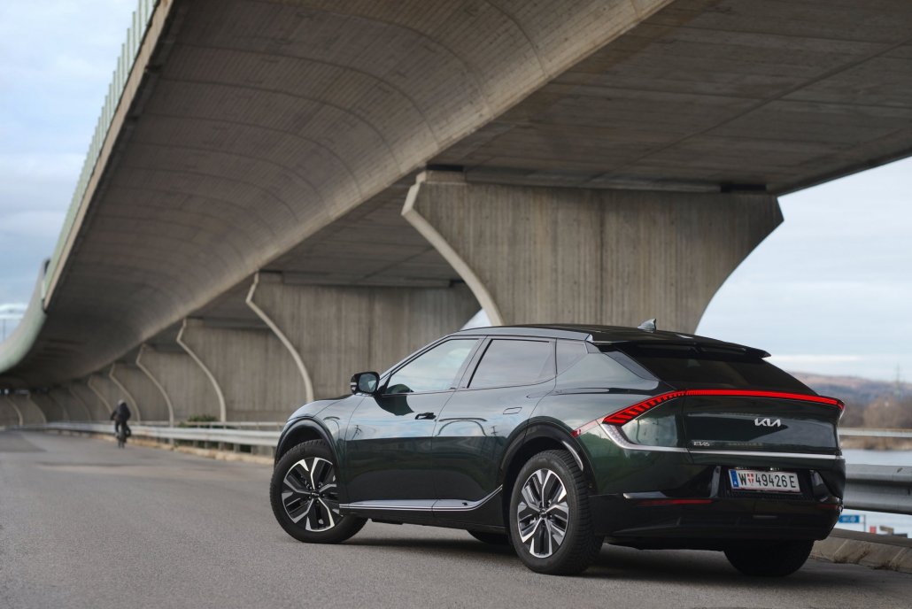 Ein dunkelgrüner Kia EV6, das Car of the Year 2022, steht auf einer Straße unter einer Brücke an einem bewölkten Tag.