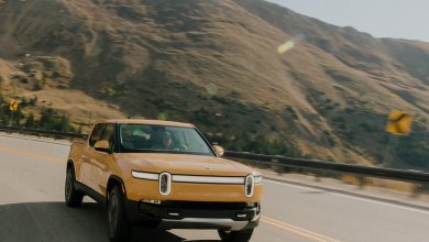 Gelber Rivian R1T fährt auf der Landstraße mit Bergen im Hintergrund