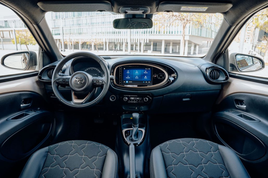 Der Innenraum eines Toyota Aygo X mit 12-Zoll-Touchscreen, Wählautomatikhebel und sportlich aussehendem Dreispeichen-Lenkrad.