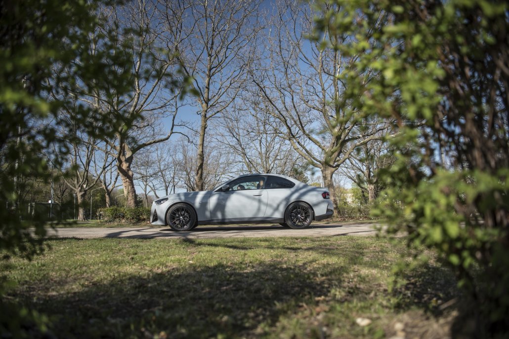 Ein graues BMW 2er Coupé steht auf Asphalt zwischen Wiesen und Bäumen