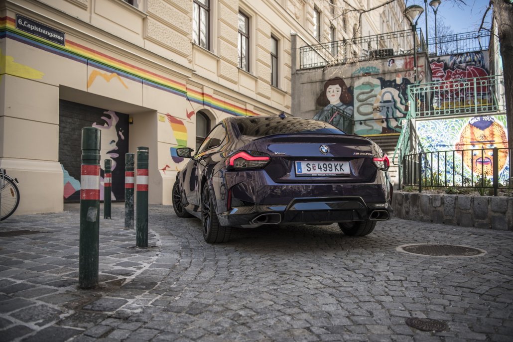 Ein BMW 2er Coupé in der Farbe Thundernight metallic steht vor einer Garageneinfahrt voller Graffiti