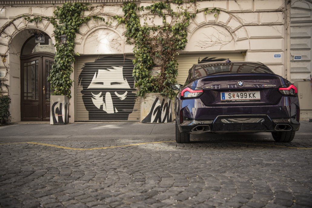 Ein BMW M240i Coupé in Thundernight metallic steht vor zwei Garageneinfahrten, die voll sind mit Graffiti