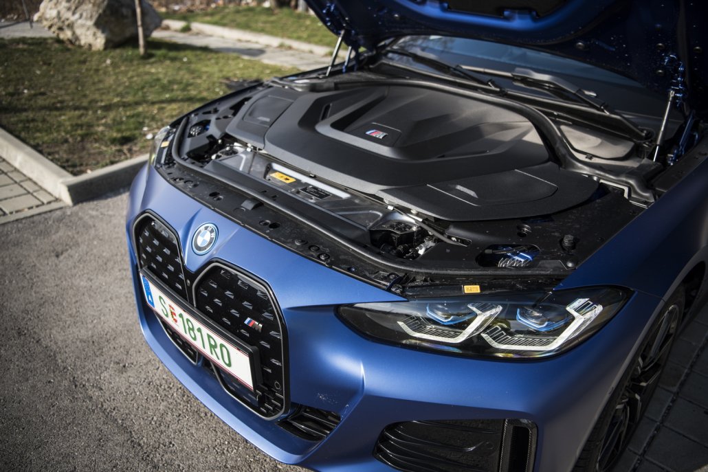 Die Motorhaube eines blauen BMW i4 M50 ist geöffnet und gibt den Blick frei auf eine große, dunkle Motorabdeckung.