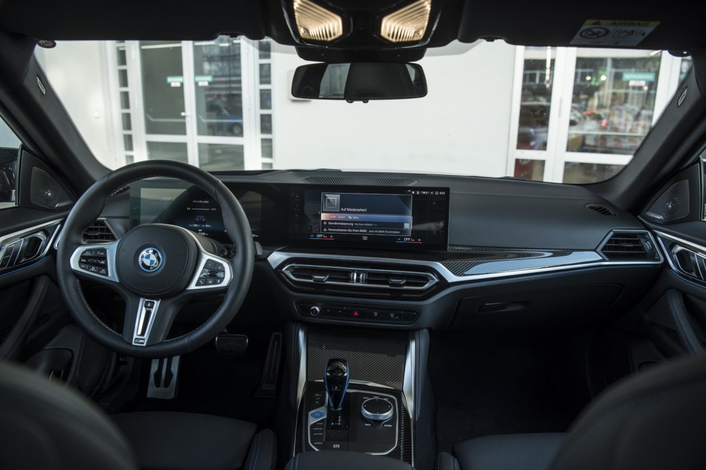Der dunkel gehaltene und mit blauen Akzentfarbenen ausgestattete Innenraum eines BMW i4 mit dem Curved Display..