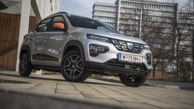 Ein silberner Dacia Spring Electric mit orangenen Akzenten steht auf einer Nebenstraße.