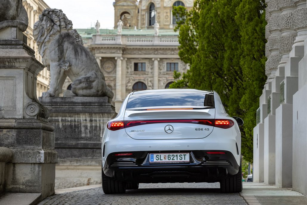 Ein weißer Mercedes EQE steht auf einem Platz zwischen einem historischen Gebäude und Löwenstatuen.