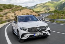 Ein weißer Mercedes GLC fährt auf einer Landstraße durch eine hügelige Landschaft