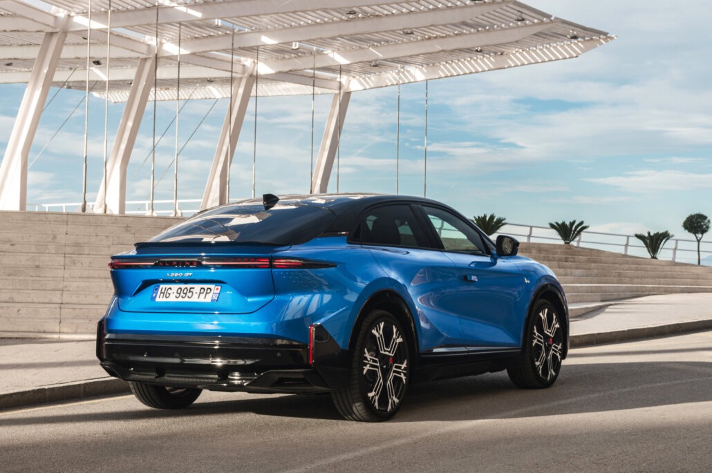 Dreiviertelansicht hinten rechts eines blauen Crossover-SUV Alpine A390_GT mit schwarzem Dach und Felgen auf einer Straße vor einer modernen Überdachung.