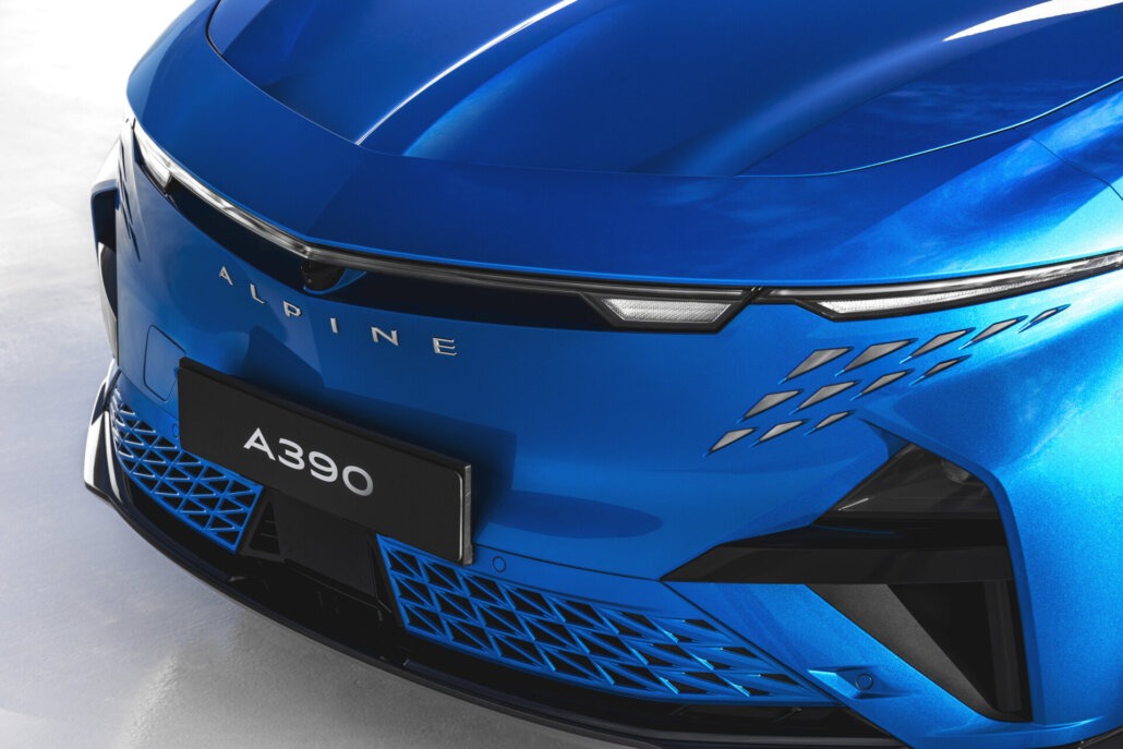 Detailaufnahme der blauen Frontpartie eines Alpine A390 mit dem lesbaren Schriftzug auf der Motorhaube und einem Kennzeichen mit Typenbezeichnung vor hellem Hintergrund.