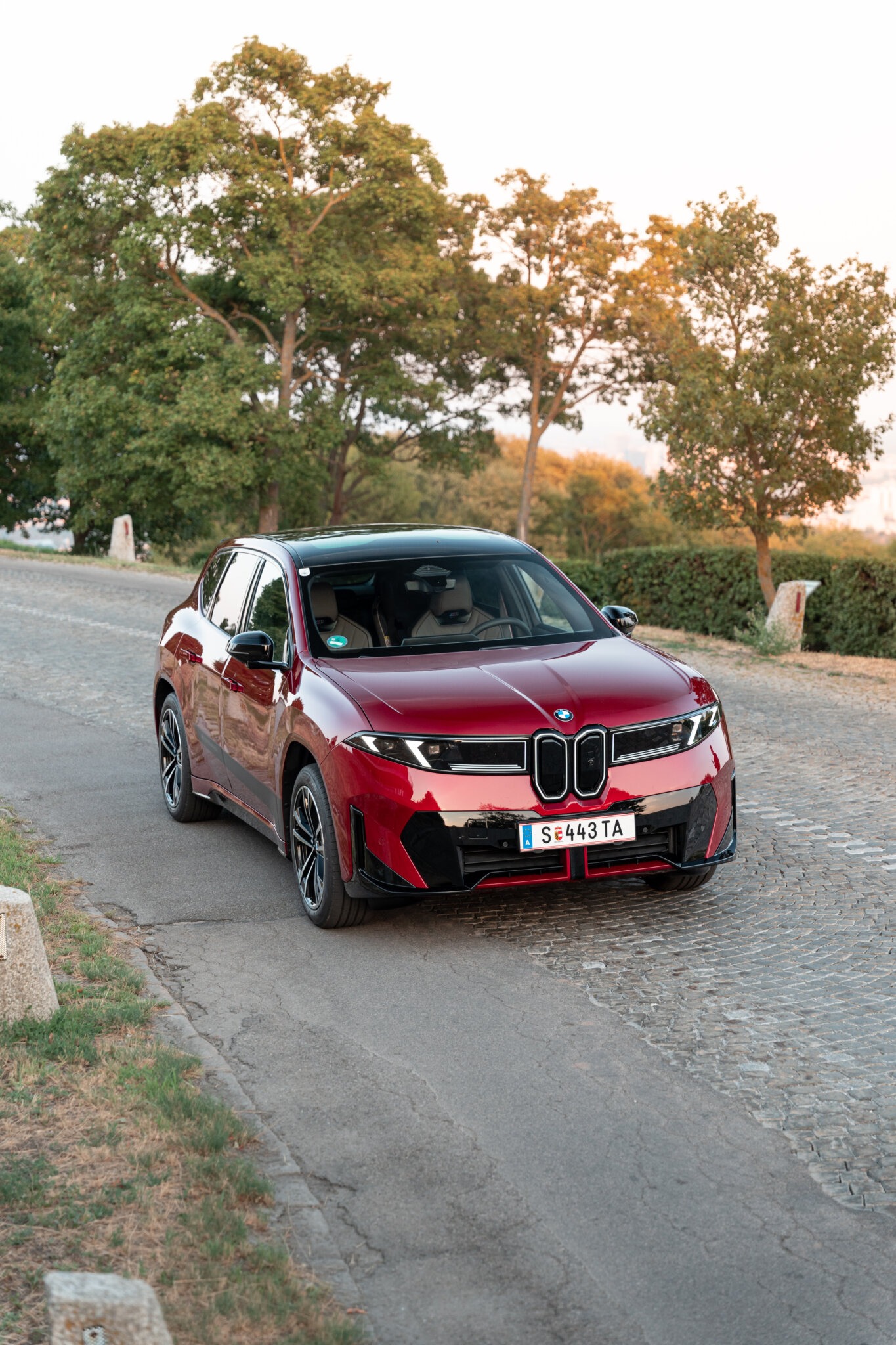 Roter BMW iX3 40 im Abendlicht auf einer Kopfsteinpflasterstraße am Stadtrand von Wien