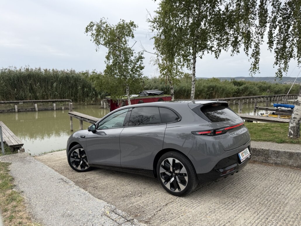 Ein dunkelgraues Leapmotor C10 SUV in Dreiviertelansicht hinten rechts steht auf einer betonierten Bootslipanlage an einem See mit Schilfgürtel und Bäumen.