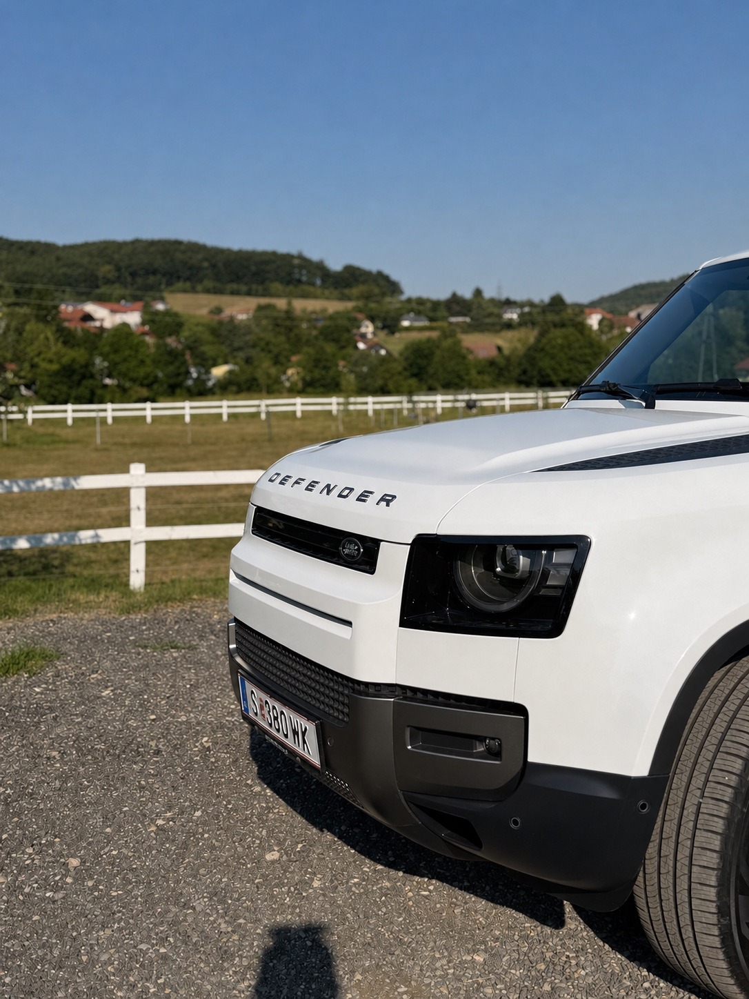Weißer Land Rover Defender auf einem Schotterweg im Grünen.
