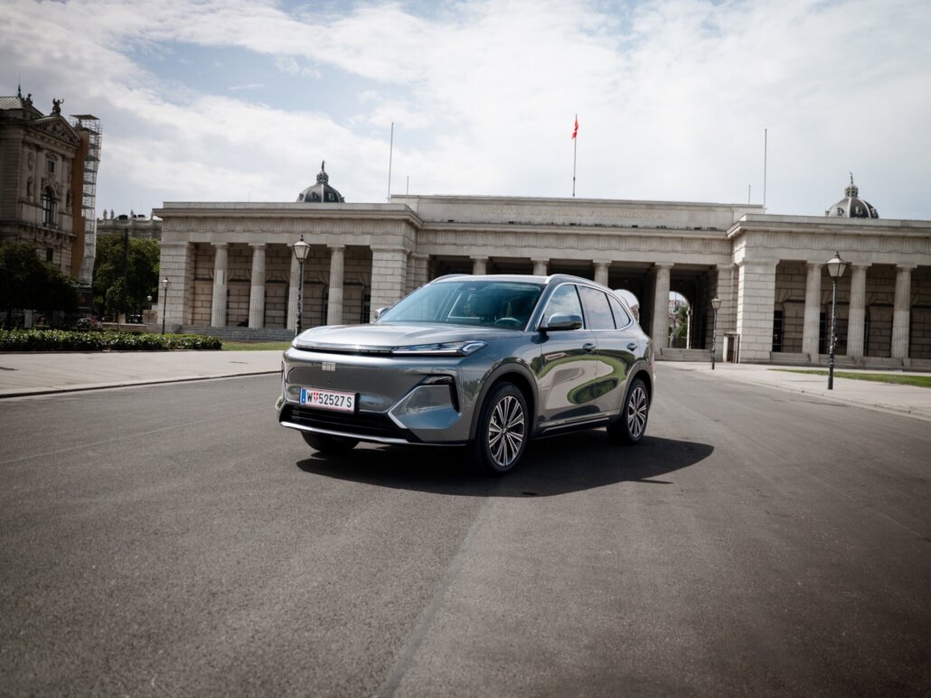 Ein grauer Kompakt-SUV in Dreiviertelansicht vorne links steht auf einer asphaltierten Straße vor einem historischen Gebäude mit Säulen.