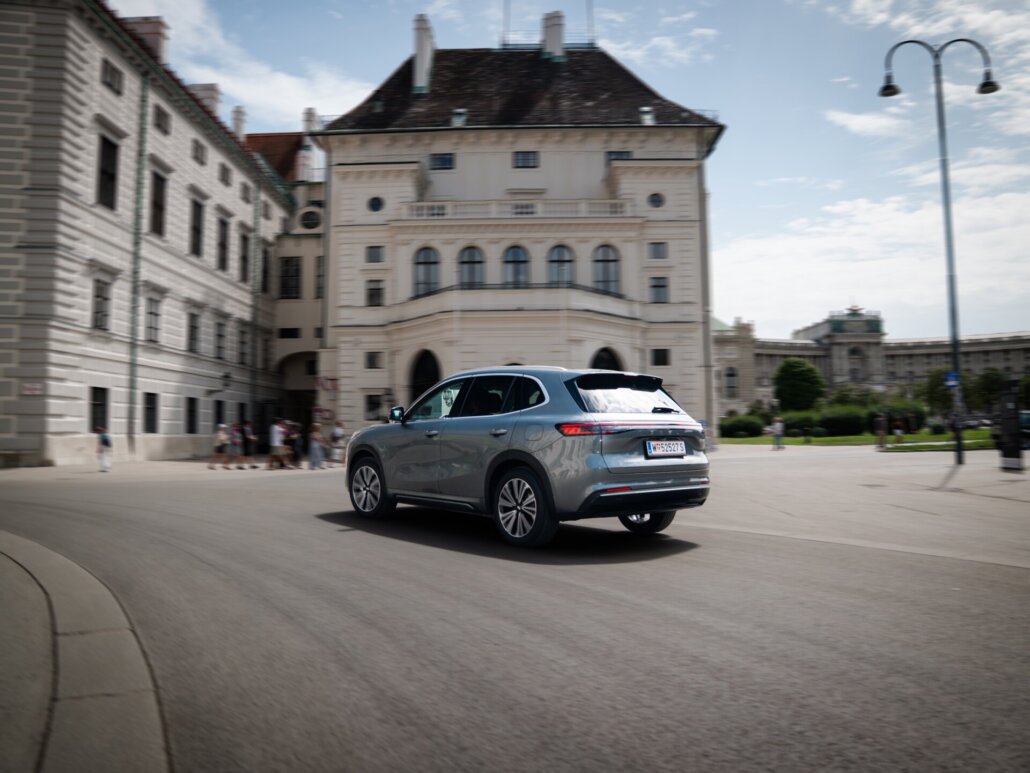 Ein grauer Kompakt-SUV ist in einer Dreiviertelansicht von hinten rechts auf einer Straße vor historischer Stadtarchitektur abgebildet.