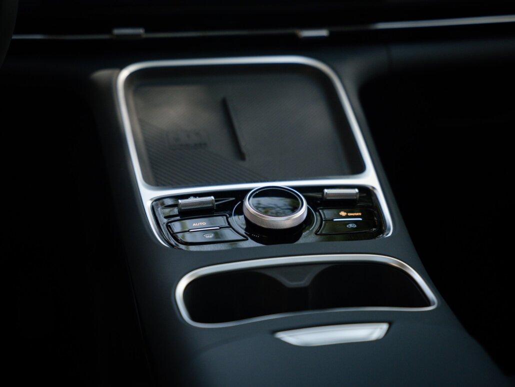 Innenraumdetail des Autos mit dem Fokus auf die schwarze Mittelkonsole, die Ablagefläche, einen Drehregler sowie Tasten mit Chrom-Akzenten.