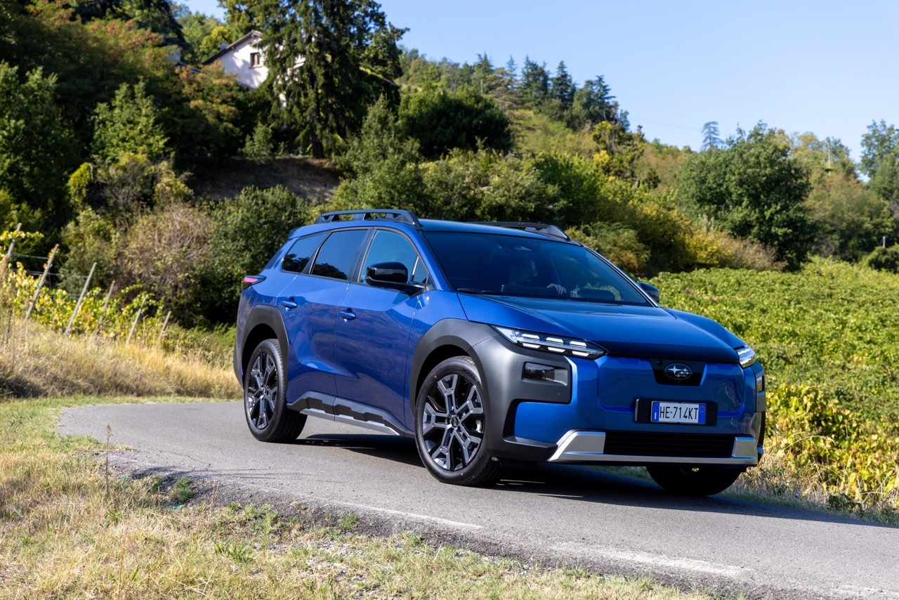 Dreiviertelansicht vorne rechts eines blauen Subaru Kompakt-SUV auf einer kurvigen Straße vor einer hügeligen Waldlandschaft.
