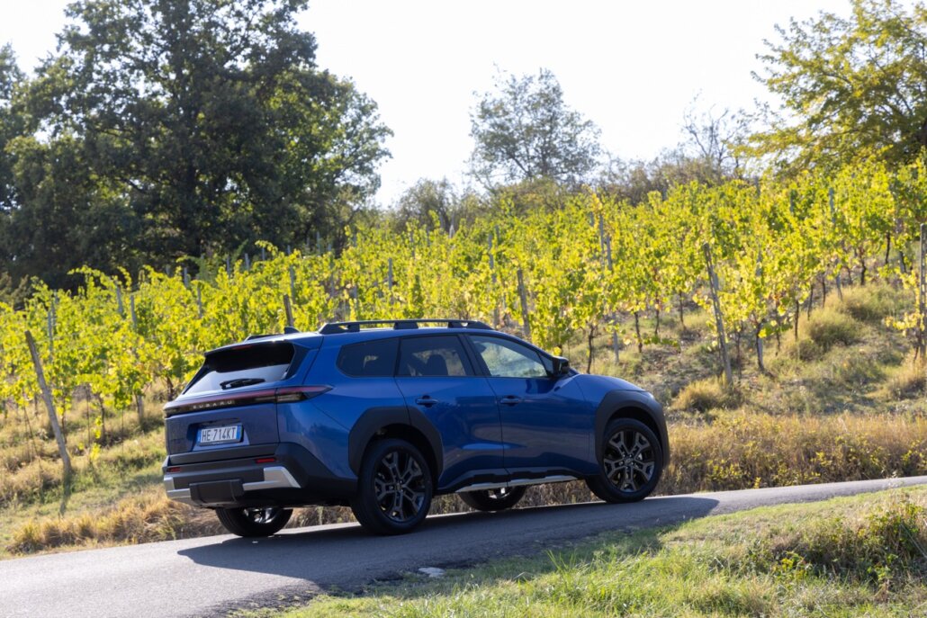 Ein blauer Subaru-Kompakt-SUV in Dreiviertelansicht von hinten rechts auf einer Landstraße vor einer Weinberg- und Waldlandschaft.