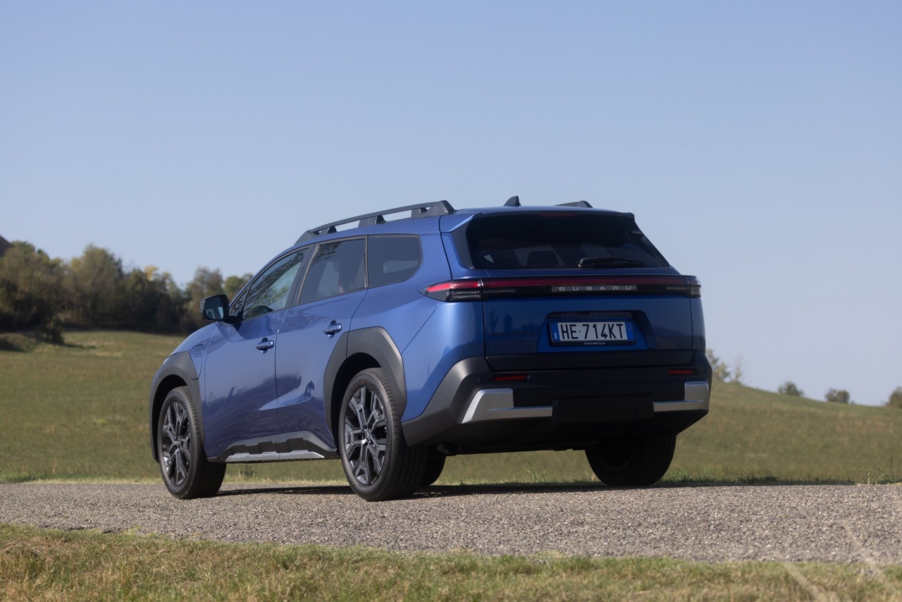 Dreiviertelansicht hinten rechts von einem blauen Subaru SUV auf einer asphaltierten Straße vor ländlicher Kulisse.