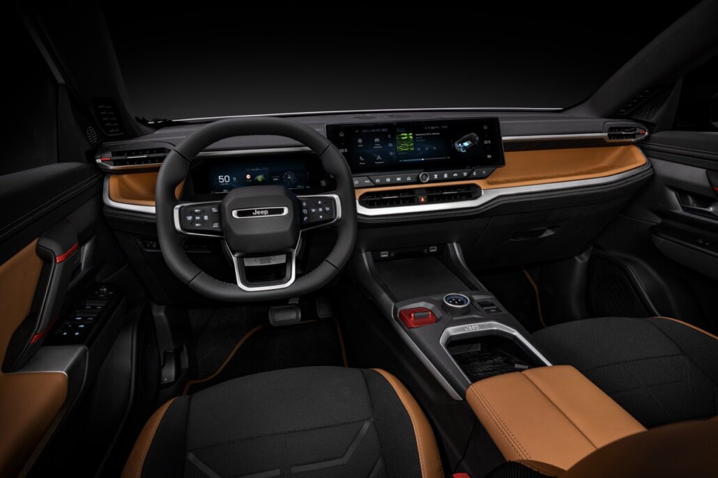 Der Innenraum eines Jeep-SUV zeigt das Armaturenbrett mit Lenkrad, Displays und schwarz-braunen Sitzen in der Totalen von vorn.