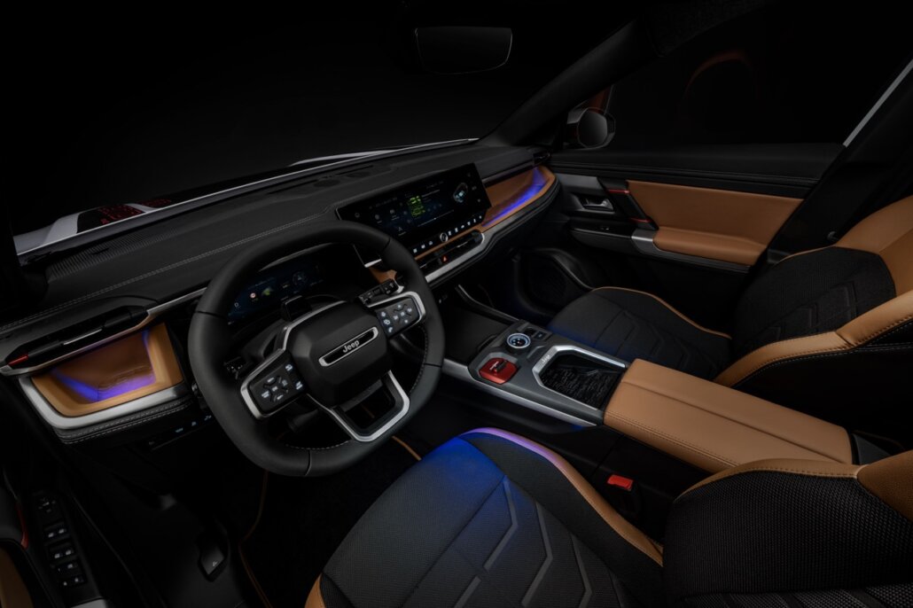 Innenraum eines Jeep-Modells mit schwarzem Lenkrad, schwarz-braunen Sitzen und digitalem Cockpit in einer Studio- oder Nachtumgebung, fotografiert aus erhöhter Perspektive von vorne rechts.