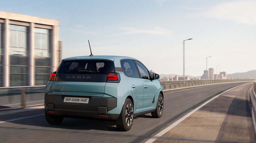 Dreiviertelansicht von hinten rechts eines hellblauen Dacia Spring Kleinstwagen-SUV auf einer Brücke.