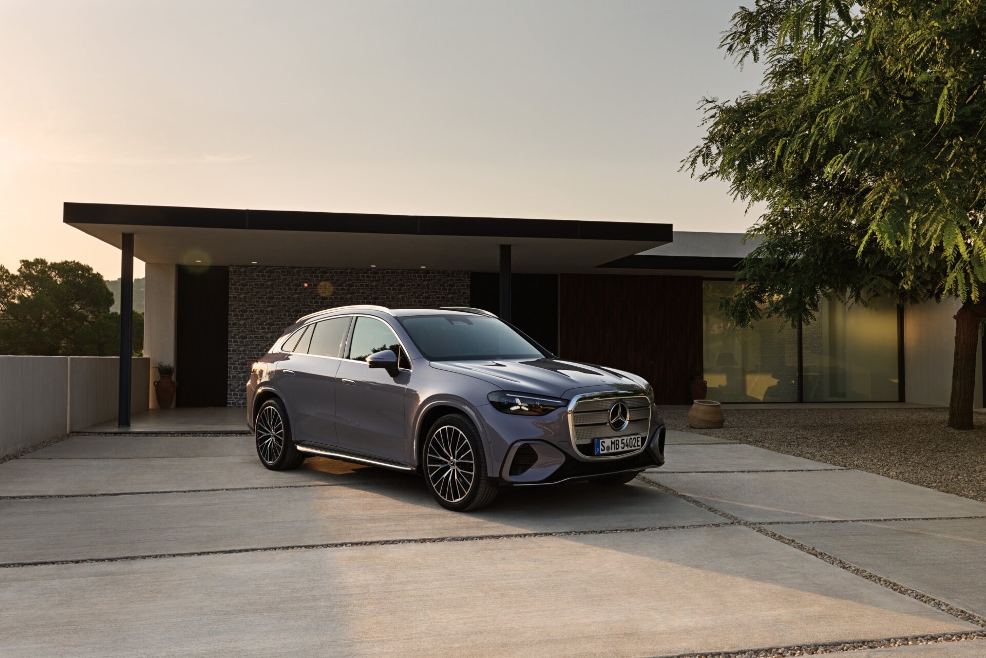 Grauer Mercedes-Benz GLC elektrisch in Dreiviertelansicht vor einem modernen Wohnhaus bei Dämmerlicht