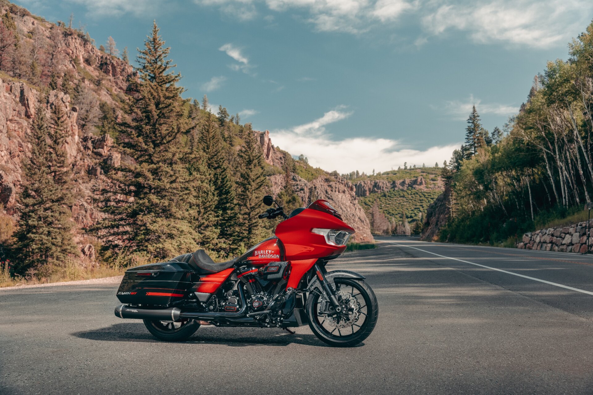 Rotes Harley-Davidson CVO Road Glide Motorrad in Seitenansicht auf einer Straße vor bergiger Waldlandschaft