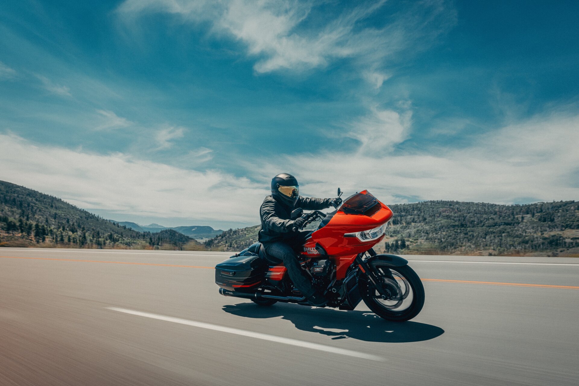 Rot-schwarzes Harley-Davidson-Touring-Motorrad in Fahrt auf einer Landstraße vor hügeliger Landschaft