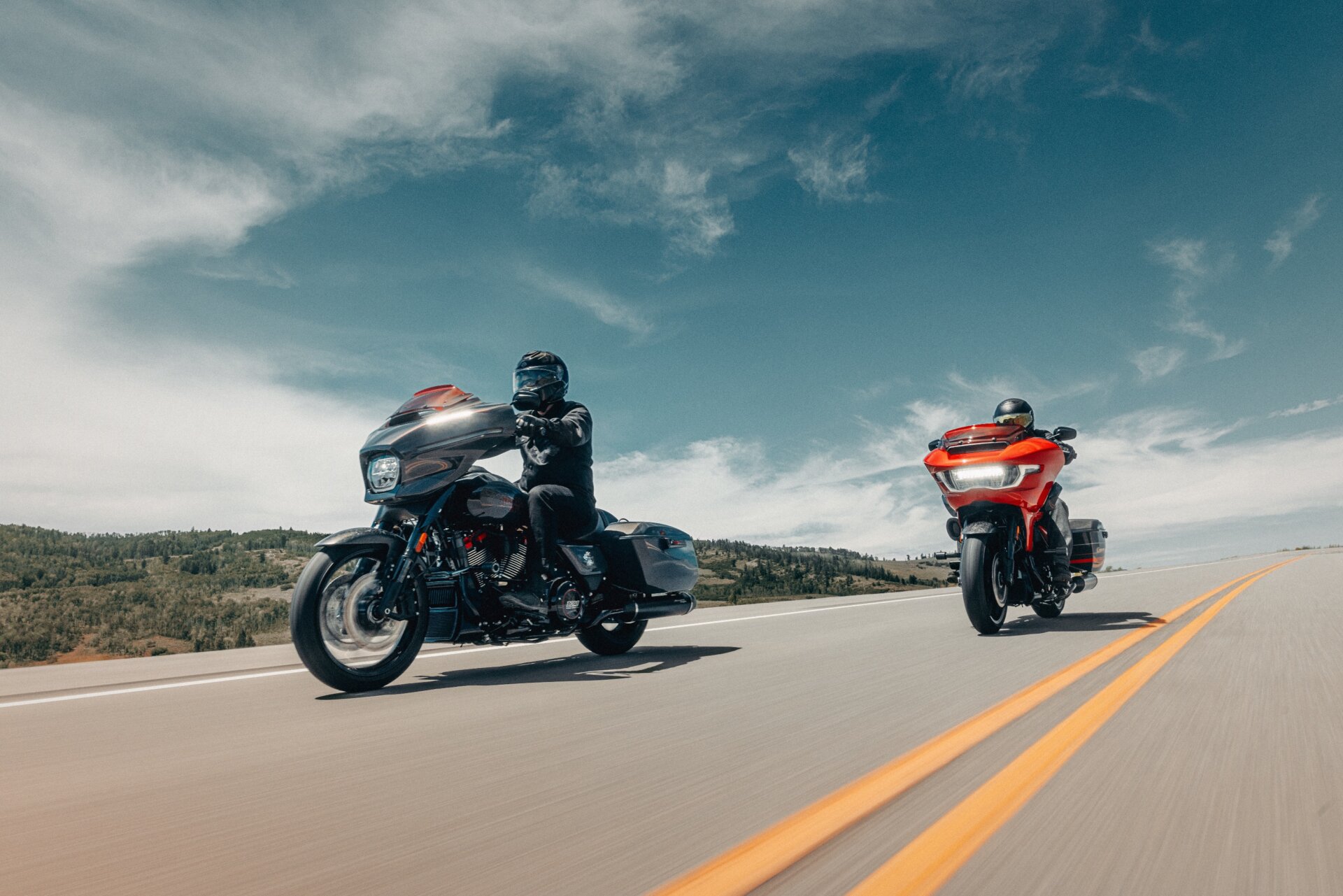 Ein dunkles und ein rotes Tourenmotorrad fahren auf einer asphaltierten Landstraße durch eine hügelige Landschaft