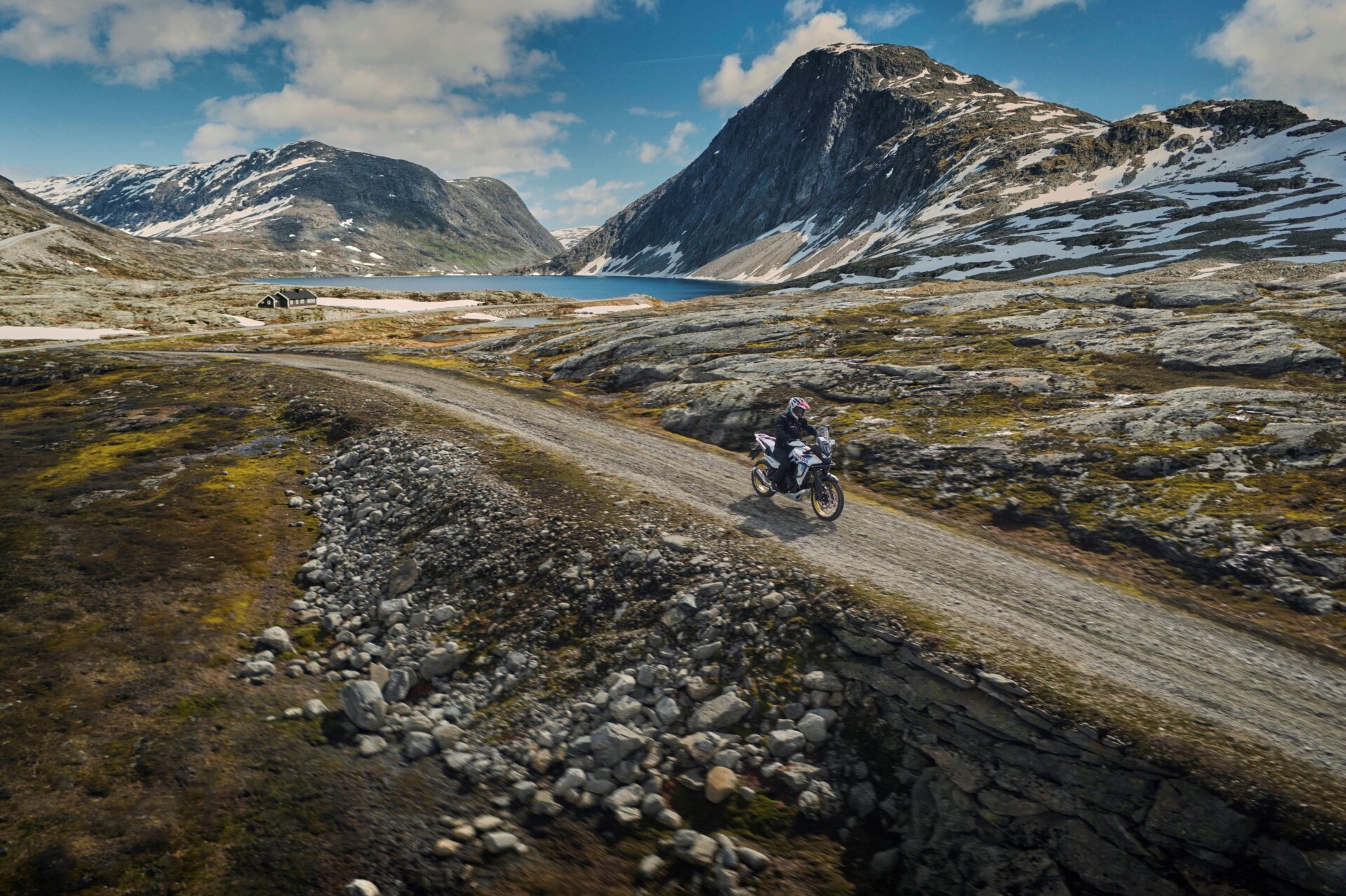 Honda Transalp Test: Motorradfahrt auf einer Schotterstraße in einer verschneiten Berglandschaft mit See