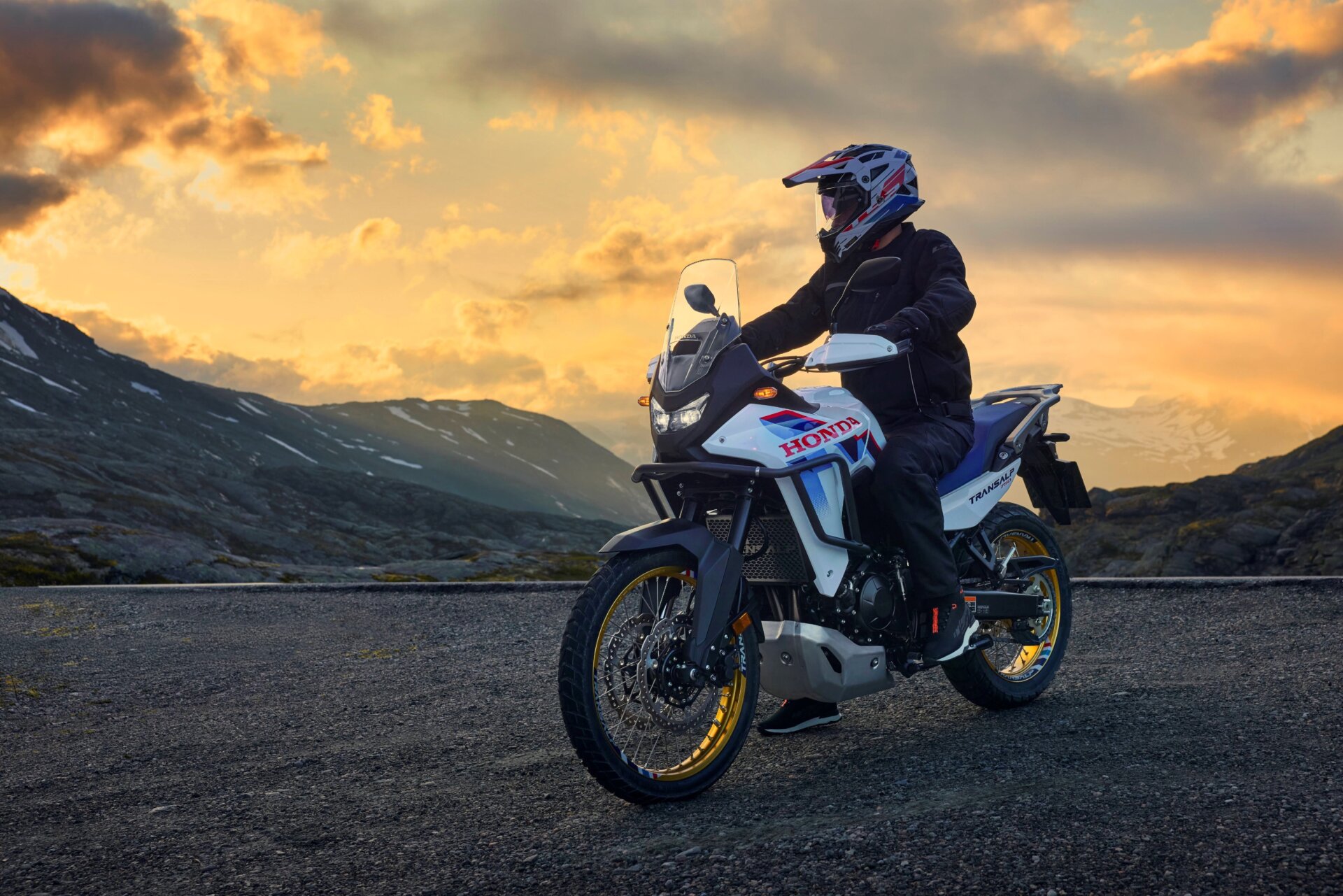 Honda Transalp Enduro vor abendlicher Bergkulisse auf einer Schotterstraße