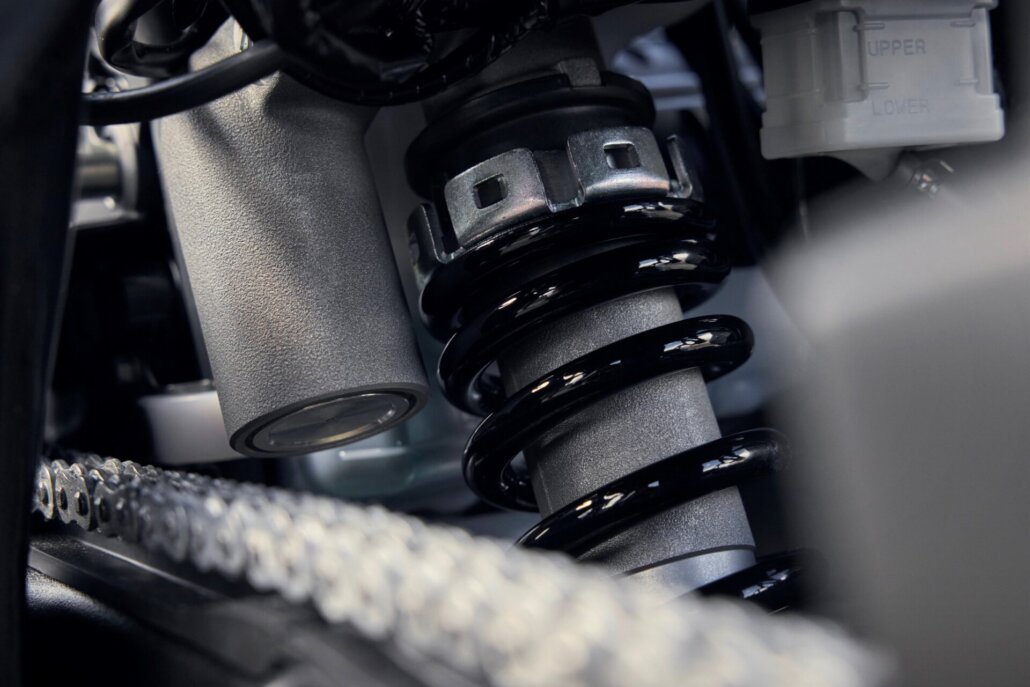 Detailaufnahme des Federbeins eines Motorrads mit silberfarbenem Dämpfer und schwarzer Spiralfeder.