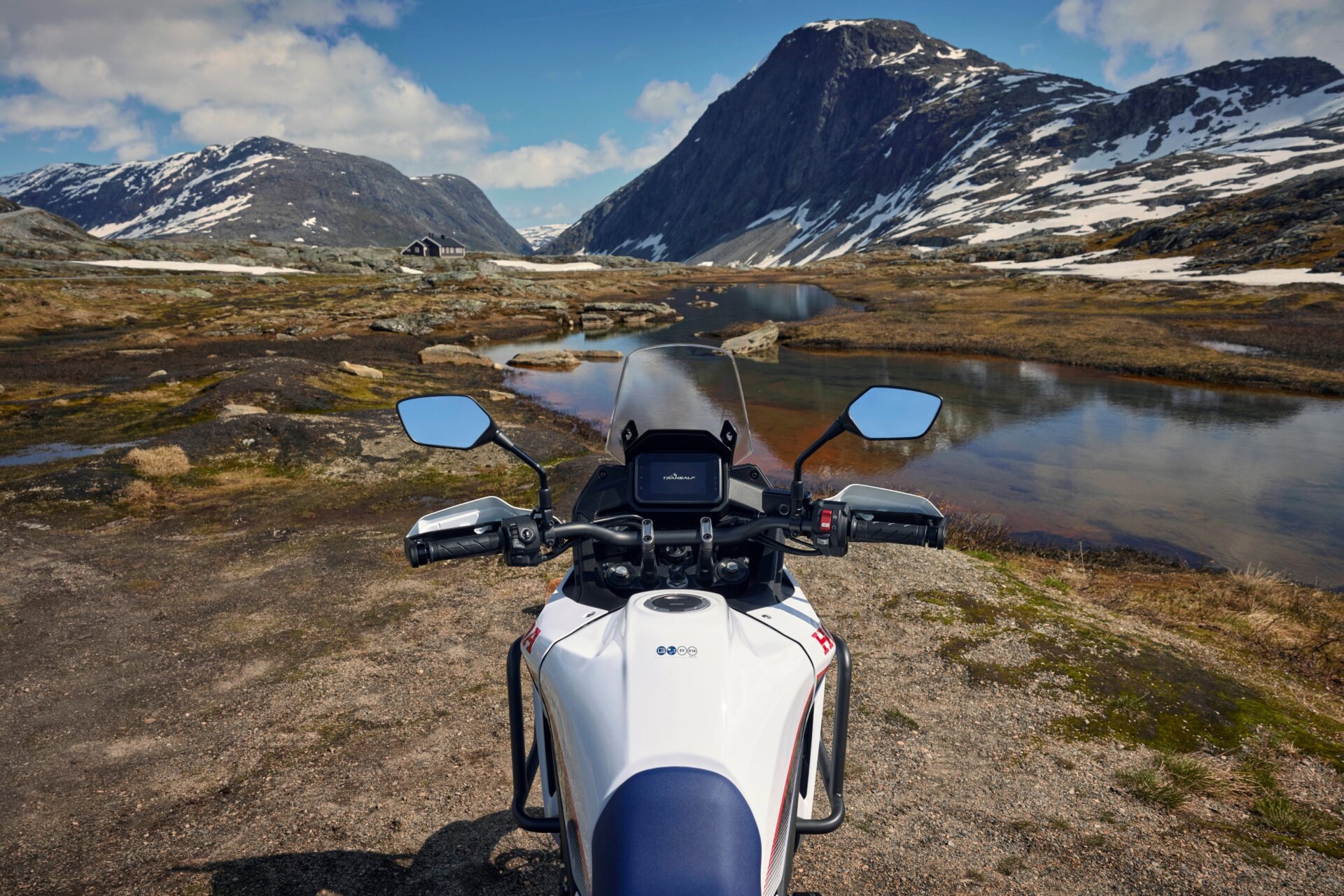 Cockpit- und Frontansicht der Honda Transalp aus Fahrerperspektive vor einer Berglandschaft mit Schnee und einem Fluss