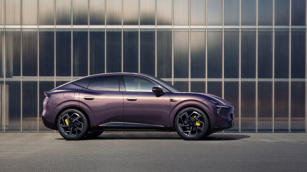 Ein lilafarbener SUV im Coupé-Design in Seitenansicht vor einer modernen Glasfassade.