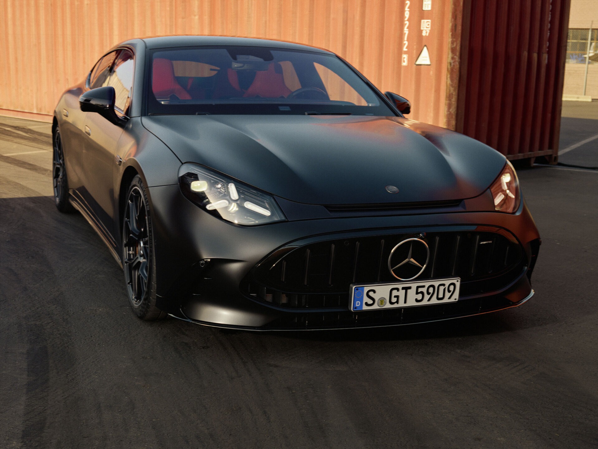 Mercedes-AMG GT 4-Türer Coupé in matter Lackierung von vorn zwischen Containern